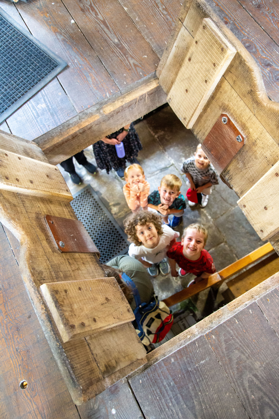 A group of people standing inside a square wooden structure with an open top, viewed from above.